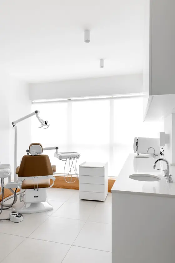 Sala clínica do consultório com cadeira odontológica, bancada e janela ampla com luz natural.
